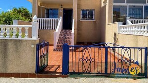 A multi-story residential building with a gated entrance, a staircase leading to the entrance, and a balcony with white railings. - 2-Bed Ground-Floor Apt in La Cinuelica R2 L188 (Orihuela)