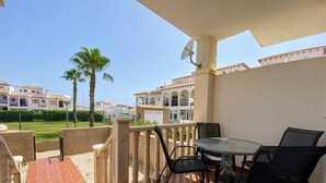 A balcony with a table and chairs, overlooking a well-maintained lawn and buildings with traditional architecture.