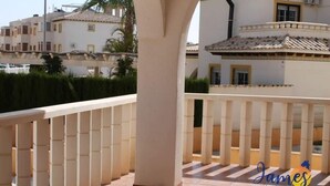 Un balcon doté d’une balustrade blanche, de piliers de couleur beige et d’un sol carrelé.