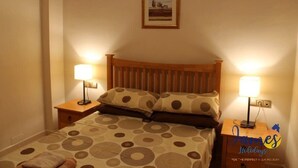 Un lit bien fait, recouvert d’une couvre-lit à motifs, avec deux lampes de chevet et un tableau encadré accroché au mur.