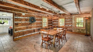 A rustic dining area with a wooden table and chairs, a brick floor, and exposed wooden beams. - Stone Creek Farm (Easton)