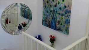 A staircase with white railings, a round mirror, and a peacock painting on the wall.