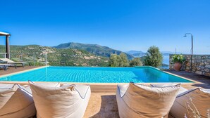 A swimming pool with a view of mountains, surrounded by lounge chairs and a stone wall. - Villa Nirvana - Alfresco Villas - Breathtaking view (Sivota)