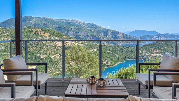 A balcony with a wooden table and two chairs, overlooking a mountainous landscape and a body of water. - Villa Nirvana - Alfresco Villas - Breathtaking view (Sivota)