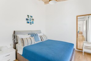 Een slaapkamer met een bed, nachtkastje, spiegel en een muur met foto's.