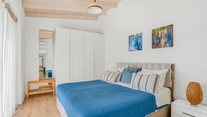 A bedroom with a large bed, a bedside table, a lamp, and two wall-mounted paintings. - Villa Nirvana - Alfresco Villas - Breathtaking view (Sivota)