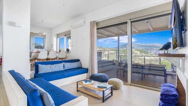 A modern living room with a blue sofa, a coffee table, and a view of a balcony with outdoor furniture.