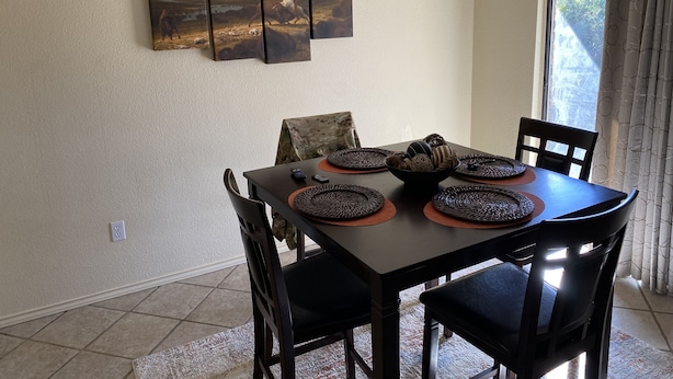 Un comedor con una mesa dispuesta para cuatro personas, rodeada de sillas. Hay tres cuadros en la pared sobre la mesa.