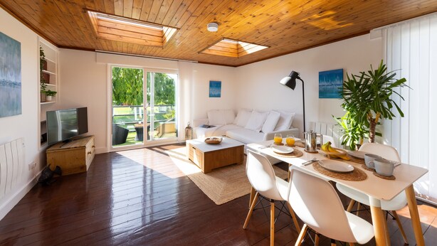 A modern living room with a wooden ceiling, a white sofa, a dining table with chairs, and a television on a wooden cabinet. - 4 Avocet Quay , Emsworth  - sleeps 4 guests  in 2 bedrooms (Emsworth)