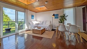 A modern living room with a wooden ceiling, a sofa, a coffee table, a dining table with chairs, and a view of greenery outside. - 4 Avocet Quay , Emsworth  - sleeps 4 guests  in 2 bedrooms (Emsworth)