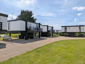 A row of modern, modular mobile homes with balconies, a gravel driveway, and a grassy area.