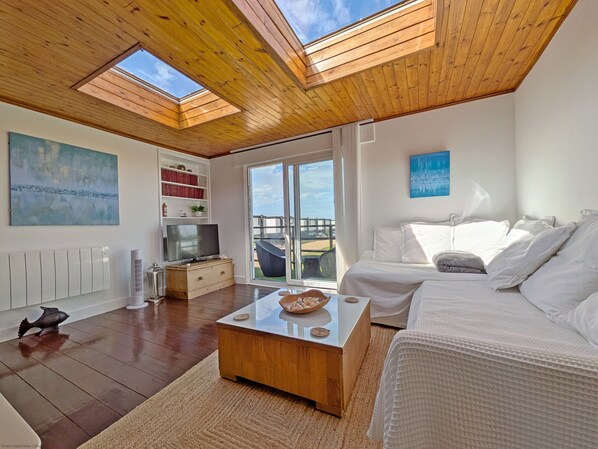 Un salon spacieux doté d’un plafond en bois, d’une télévision, d’un canapé et d’une grande fenêtre donnant sur un paysage agréable.