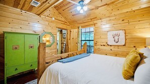 Une chambre dans une cabane en bois, avec un lit, une armoire verte et un ventilateur de plafond.
