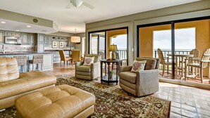 A spacious living area with leather sofas, a dining table, and chairs, a kitchen with cabinets, and a balcony with chairs.