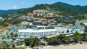 Een kustplaats met een opvallend hotel met een modern design, nabij een strand en omringd door weelderige begroeiing en heuvels.