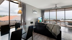 Een moderne woonkamer met een glazen eettafel, een leren bank in zwart leer, en een grote televisie.