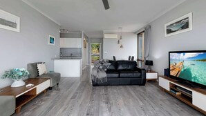 Een moderne woonkamer met een grijze bank, een flatscreen televisie en een plafondventilator.