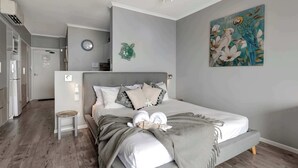 A modern bedroom with a grey bed, white pillows, and a grey throw blanket. There is a painting of parrots on the wall.