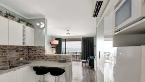 A modern kitchen with a brick backsplash, white cabinetry, and a bar area with stools.