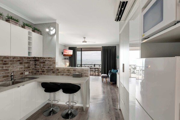 A modern kitchen with a brick backsplash, white cabinetry, and a bar area with stools.