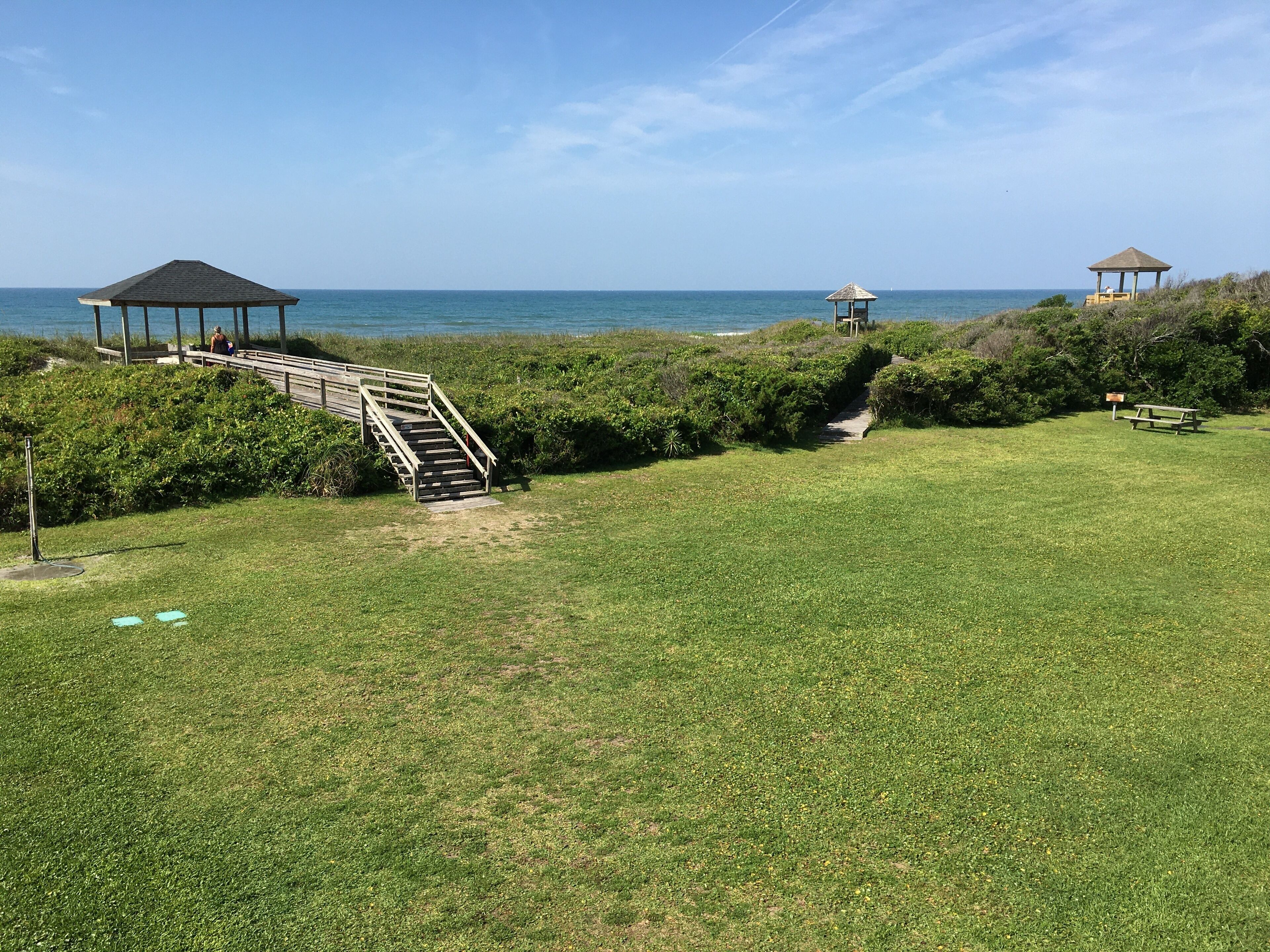 Uma área gramada com uma escadaria de madeira que leva a um gazebo à beira-mar.