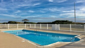 Ein Schwimmbecken mit weißem Zaun, einer Laube und blauem Himmel.