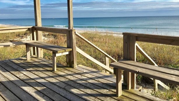 Eine Holzterrasse mit Bänken mit Blick auf einen Strand.