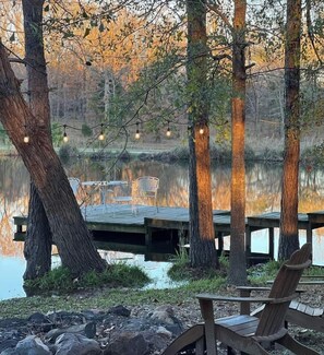 Terraza junto al lago con sillas y mesas de madera, rodeada de árboles y una masa de agua tranquila.