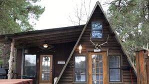Una cabaña de madera con un porche, un espacio de estar cubierto al aire libre y una pequeña terraza.