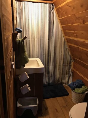 Un baño pequeño con paneles de madera, un lavamanos, un perchero para toallas y una cortina de ducha.