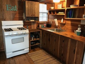 A kitchen with wooden cabinets, a stove, a sink, and a window. - The Bluegill Aframe cabin at Bluegill Lake Cabins (Eustace)