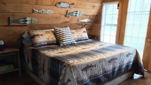 Un dormitorio de cabaña de madera con una cama, almohadas y decoración de peces en la pared.