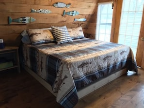 Un dormitorio de cabaña de madera con una cama, almohadas y decoración de peces en la pared.