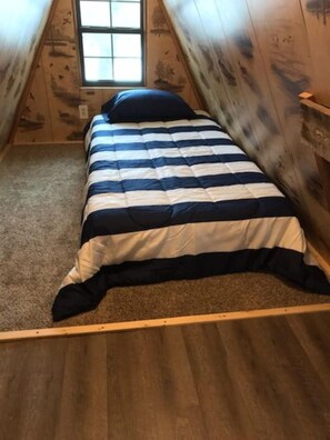 Una cama individual en una habitación con paredes de madera y techo inclinado.