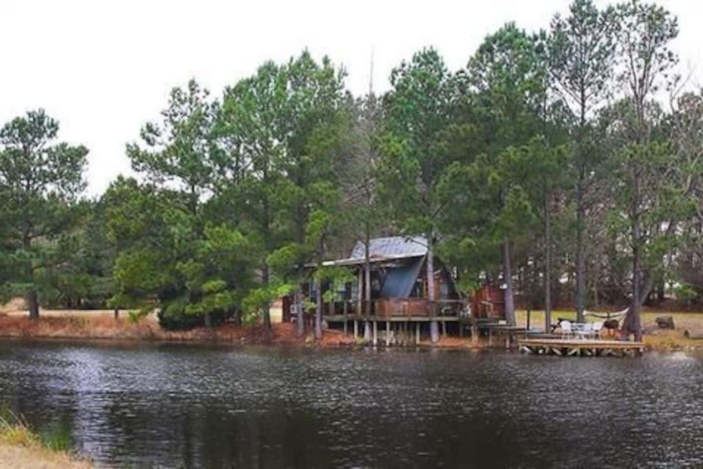 Une cabane au bord d’un lac, entourée d’arbres.