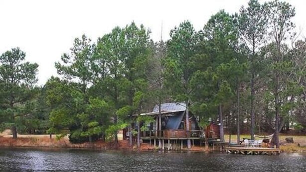 Una cabaña junto a un lago rodeada de árboles.