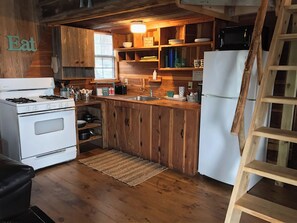 Kitchen features a stove, sink, and refrigerator, with wooden cabinetry and a lofted area.