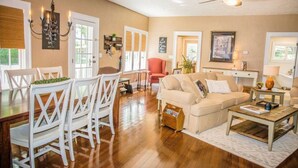 A spacious living room with a wooden floor, a beige sofa, white chairs, a dining table with chairs, and a ceiling fan. - Beautiful Branson Home! Perfect Downtown Location! (Branson)