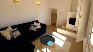 En moderne stue med en mørkeblå sofa, et glasbord og to vægmonterede lamper.
