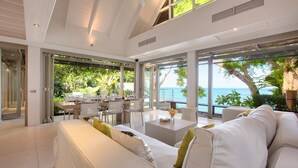 A spacious living area with a large white sofa, a dining table set for a meal, and a view of the ocean through large windows. - The Headland Villa 2, stunning beachfront, Samui (Koh Samui)
