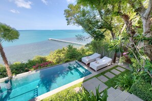 Piscina privada con dos sillas reclinables blancas y una terraza de madera.