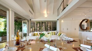 A dining area with a wooden table set for a meal, white furniture, and a view of greenery outside. - The Headland Villa 2, stunning beachfront, Samui (Koh Samui)