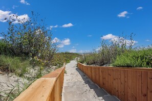Un paseo marítimo de madera que atraviesa un paisaje natural con arena y vegetación.