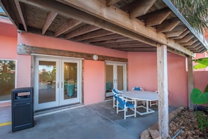 Une terrasse couverte avec une table et des chaises, une poubelle et une porte-fenêtre coulissante.