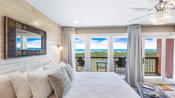A bedroom with a large bed, a ceiling fan, a decorative mirror, and a view of the ocean through a sliding glass door. - Beachfront Boutique Resort  |  Coastal Retreat  |  Casa Condo 203 (Port Aransas)