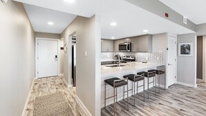 A modern kitchen with a central island, bar stools, and a microwave. - Beachfront Boutique Resort  |  Coastal Retreat  |  Casa Condo 203 (Port Aransas)