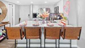 Una cocina moderna con armarios blancos, un refrigerador de acero inoxidable y una luz de neón con forma de corazón en la pared.