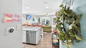 Una cocina moderna con una isla central, un comedor con un sofá verde y una sala de estar con un ventanal grande.