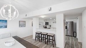 A modern kitchen with white cabinets, a stainless steel refrigerator, and a bar area with stools. - Beachfront Boutique Resort |Serene Escape| Casa Condo 210 (Port Aransas)