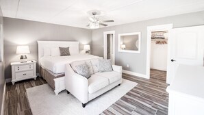 A bedroom with a large bed, a white sofa, a ceiling fan, and a nightstand with a lamp. - Beachfront Boutique Resort |Serene Escape| Casa Condo 210 (Port Aransas)